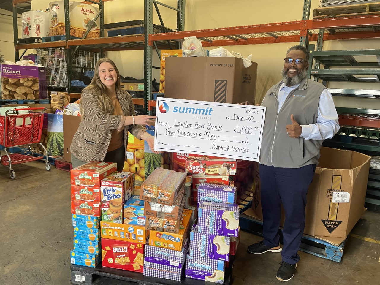 Two people stand with a large check and boxes of donated food