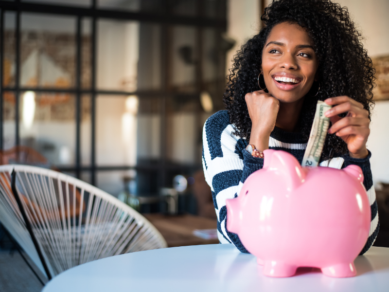 Woman next to pink piggy bank holding cash